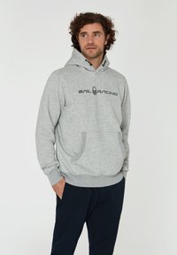 Sudadera gris con bolsillo canguro y puños acanalados. Presenta el texto "SAIL RACING" impreso en negro en la parte frontal, elaborada con una tela suave y texturizada.
