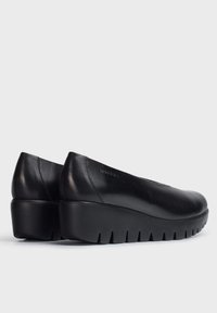 Zapatos de cuero negro con punta redondeada y tacón de cuña. Presentan una textura suave y una suela de goma con un diseño segmentado.