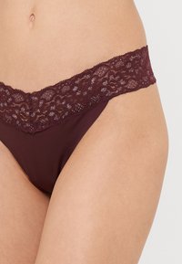 Burgundijas stringi ar plašu mežģīņu jostu ar sarežģītiem rakstiem. Gluds, viegls materiāls lieliski papildina mežģīņu akcentus.