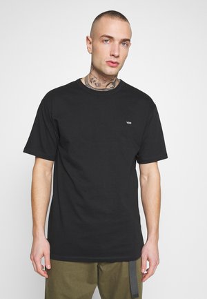 Camiseta de algodón negra con cuello redondo, mangas cortas y un pequeño logo blanco de Vans en el lado izquierdo del pecho. Diseño sencillo, de un solo color.