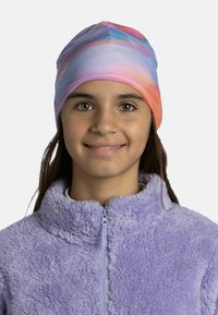 Colorful stretch beanie in shades of pink, blue, and purple, adorned with a logo. Worn with a soft, purple, zippered fleece jacket.