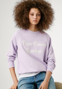 Svetlofialová mikina s nápisom "Pepe Jeans London" bielym kurzívou, rebrovanými manžetami a voľným strihom, spárovaná s džínsami.