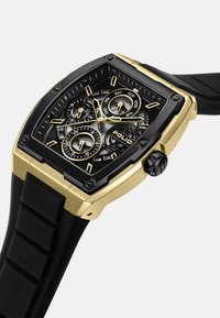 Vierkante horloge met een zwart en gouden kast, zwarte rubberen band, multi-dial weergave en metalen accenten; beschikt over dag- en datumaanduidingen.