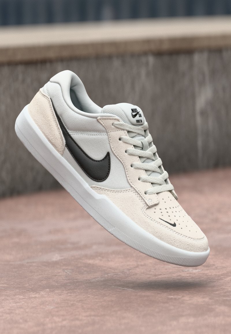 Nike SB tenisice u svijetlo sivoj i kremasto-bijeloj boji, s gornjim dijelom od antilopa, crnim swoosh logotipom, teksturiranim detaljima i bijelim gumenom potplatom.