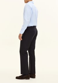 Himmelblaues Langarmhemd kombiniert mit schwarzen Anzughosen. Das Outfit verfügt über einen klassischen Kragen und subtile Knopfdetails. Braune Wildleder-Loafers runden den Look ab.