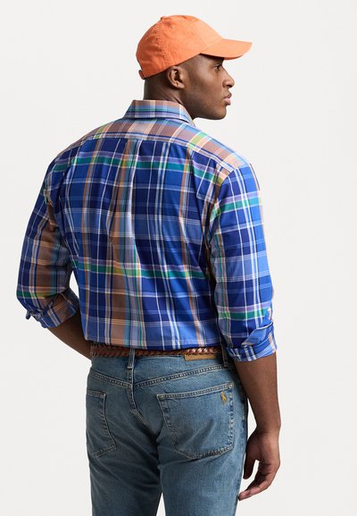 Blå og brun rutete skjorte med opprullede ermer, kombinert med lyseblå jeans og en oransje caps, med et flettet brunt belte.