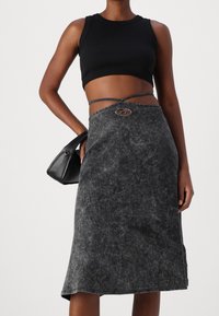 Schwarzes Crop-Top mit geripptem Material, kombiniert mit einem grauen, strukturierten Midikleid mit einem dekorativen Gürtelschlaufen und einer schlichten schwarzen Handtasche.
