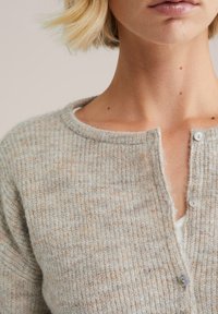 Cardigan côtelé gris clair et beige en tricot doux, avec un col rond et une fermeture par boutons discrets.
