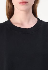 Μαύρη φούτερ μπλούζα με ραμμένο λαιμό, από βαμβακερό ύφασμα με μαλακή υφή και απλό, κλασικό σχέδιο.