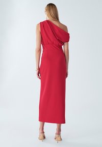 Robe rouge moulante à une épaule, confectionnée dans un tissu lisse, avec un design drapé et une silhouette longue et élégante.