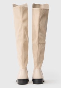 Beige ruskind over-knee støvler med en glat læderbund, der har en rund tå og en lav, stablet sort hæl.