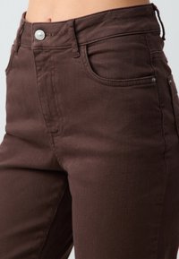 Bruine denim broek met een aansluitend ontwerp, hoge taille, een knoopsluiting en voorzakken met subtiele stikdetails.