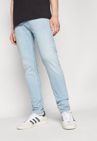 Jeans de tiro Slim de color azul claro, confeccionados en denim, con un efecto desvaído y costuras simples; combinados con zapatillas blancas con rayas oscuras.