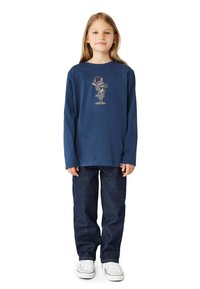 Marineblaue Langarmshirt mit einem Wolfsmotiv in der Mitte, kombiniert mit blauen Jeans und weißen Sneakers. Einfaches, lässiges Design.
