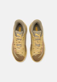 Scarpe sportive color talpa e oro con materiali in rete e sintetici, dotate di sei fori per i lacci, branding prominente e design della suola curvilinea.