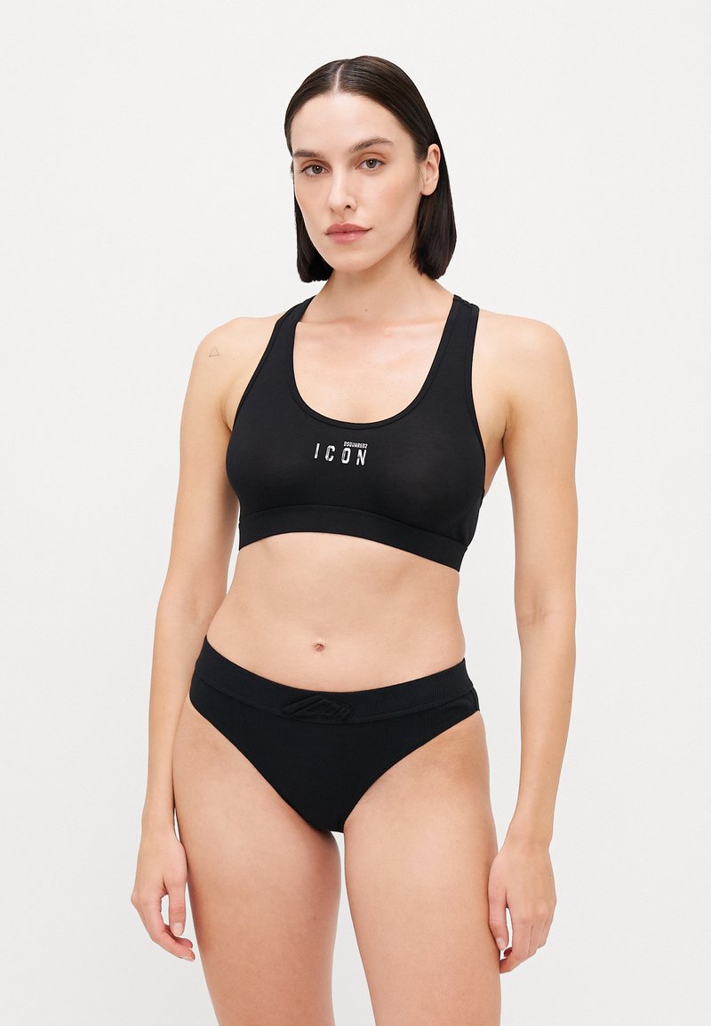 Black sports bra with thick straps and front logo; paired with black bikini-style briefs featuring a textured waistband.