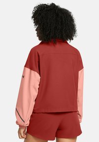 Rote und pinke Jacke mit Kragen, langen Ärmeln und elastischen Bündchen, aus glattem Stoff, mit einem Logo auf dem linken Ärmel.