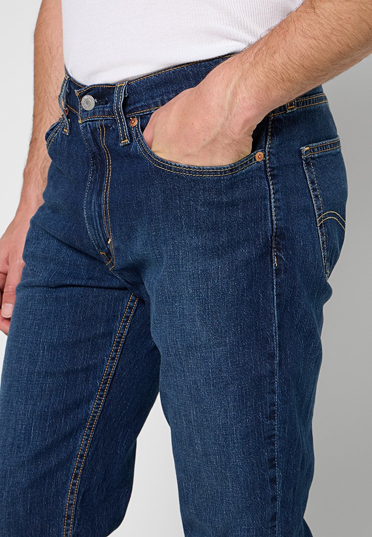 Dunkelblaue Denim-Jeans mit einem klassischen Fünf-Taschen-Design, subtilen goldenen Nähten und einem Messingknopfverschluss an der Taille.