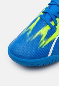 Scarpa da atletica blu con tomaia in rete testurizzata, caratterizzata da vivaci dettagli gialli a zigzag. Inclusi lacci blu e colletto imbottito.