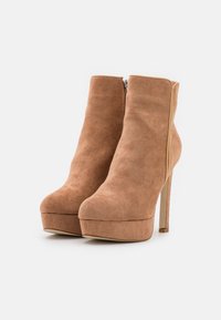 Bottines en daim marron avec un talon aiguille haut et une semelle plateforme. Dotées d'une fermeture éclair latérale et d'une texture lisse. Design à bout arrondi.