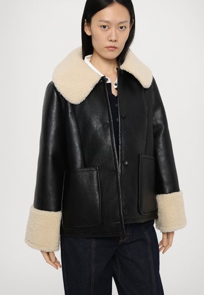 Zwarte leren jack met een grote beige schapenvacht kraag en manchetten. Voorzien van twee zakken aan de voorkant en een knopen/sluiting. Zachte textuur en oversized pasvorm.