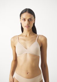 Wireless, beige bralette with a v-neck design, adjustable straps, and smooth fabric for comfort. Minimalistic style with no embellishments.