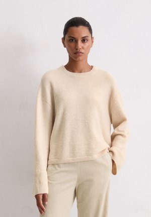 Lichtbeige gebreide trui met een ronde halslijn, verlaagde schouders en lange mouwen. Zachte textuur. Gepaarde met crèmekleurige corduroy broek.