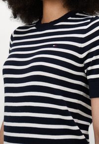 Pruhovaný svetr v námořnické modři a bílé barvě s kulatým výstřihem a krátkými rukávy. Malý detail s logem na hrudi. Měkká textura.