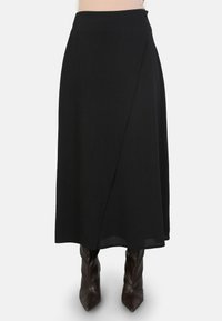 Jupe portefeuille noire en tissu léger, avec un ourlet au genou et une fermeture à bouton sur le côté. Associée à des bottes marron à hauteur du genou.