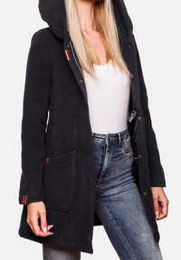 Cappotto nero con cappuccio realizzato in tessuto morbido, con chiusura a zip e bottoni a pressione, due tasche frontali e sottili dettagli in pelle marrone.