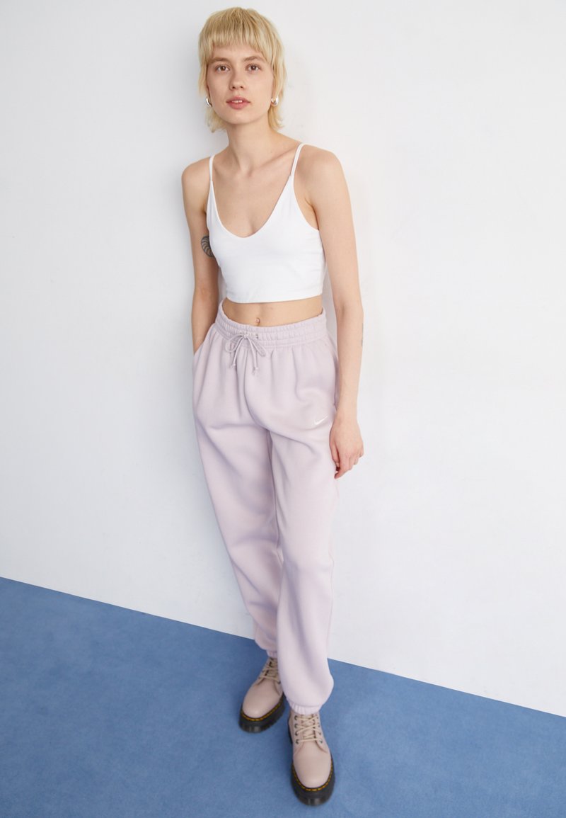 Helle lila Sweatpants mit elastischem Bund und Kordelzug, kombiniert mit einem weißen V-Ausschnitt-Crop-Top und beigen Schnürstiefeln.