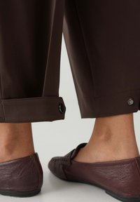 Bruine broek tot aan de enkels met knoopmanchetten, gecombineerd met donkerbruine leren loafers met gestructureerde accenten.