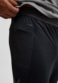 Pantalones cortos deportivos negros con una textura suave, cintura elástica y un pequeño logo "BEECOOL" en la parte trasera, con un diseño ligero.