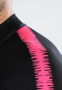 Schwarzes Sportoberteil mit einem pinken grafischen Streifenmuster auf der Schulter. Glatte Textur mit einer figurbetonten Form, aus dehnbarem Material gefertigt.