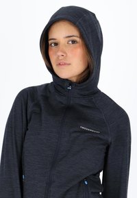 Dark blue zip-up hoodie with a high collar and hood, featuring a textured fabric and a logo on the left chest. Accented zippers in blue.