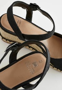 Sandales plateforme noires en toile avec une semelle de style espadrille, dotées de brides ajustables et d'une semelle intérieure beige avec un logo en relief.