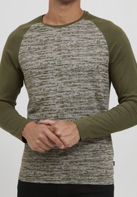 Långärmad t-shirt med en grå texturerad kropp och olivgröna ärmar. Tillverkad av ett mjukt material med rundad halsringning och subtila mönsterdetaljer.