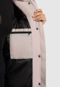 Svetloružová zateplená bunda s čiernou podšívkou, s vreckom na zips na ľavej strane a patentkami pozdĺž okraja.