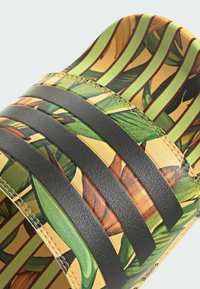 Sandal med slide-design, prydet med et grønt og gult bladmønster, sorte læderstropper og en tekstureret overflade med en glat finish.