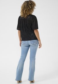 Black lace top with short sleeves, keyhole back detail, paired with light blue flared jeans, featuring stitched back pockets.
