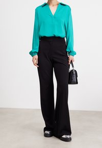 A turquoise, long-sleeve blouse with a V-neck and cuffed sleeves paired with black, wide-leg trousers. Accessories include a small black bag.