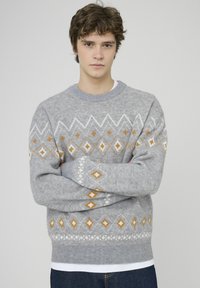 Pull gris avec un motif abstrait de losanges blancs et orange, doté d'un col rond et de poignets côtelés, fabriqué en matière tricotée douce.