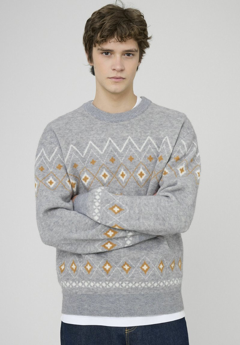 Pull gris avec un motif abstrait de losanges blancs et orange, doté d'un col rond et de poignets côtelés, fabriqué en matière tricotée douce.