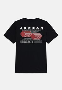 T-shirt en coton noir avec un design graphique comportant des formes géométriques rouges et le texte "JORDAN" au dos. Manches courtes et col classique.