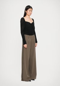 Sort langærmet bluse med samlet tekstur, parret med højtaljede brune brede bukser med sidedejepunkt.