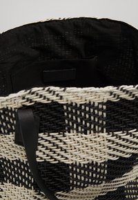Schwarz-weiße geflochtene Tragetasche mit diagonalen Muster, offenes Oberteil zeigt schwarze Stoffauskleidung und kleine Innentasche.