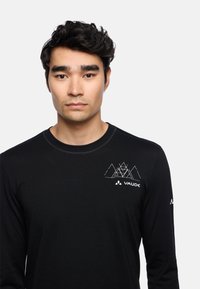 Zwarte T-shirt met lange mouwen van zacht materiaal, met een witte geometrische bergafbeelding en het "VAUDE" logo op de borst.