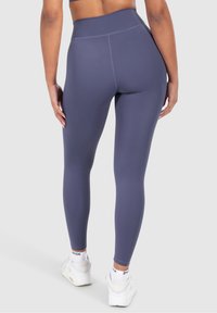 Leggings a vita alta in tessuto grigio scuro con una texture liscia. Design aderente con cuciture rinforzate, abbinati a sneakers bianche.