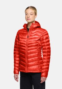 Giubbotto isolato rosso con motivi a rombi orizzontali e diagonali, chiusura con zip e cappuccio. Il materiale sembra lucido e leggero.