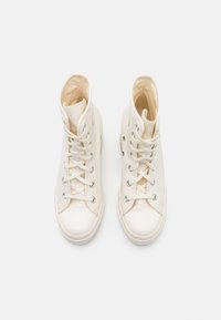 Paire de baskets montantes en toile blanc cassé avec embouts en caoutchouc blanc et lacets, vues de dessus sur fond blanc.